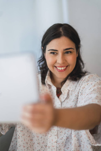 A vertical shot of a smiling Spanish girl using a tablet indoors - Fotografie, Obrázek
