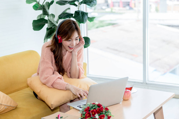 Portré képek ázsiai vonzó nő ül a kanapén, visel fülhallgató és a munka otthonról, amely használja notebook számítógépek, dolgozni otthonról és üzleti online koncepció - Fotó, kép