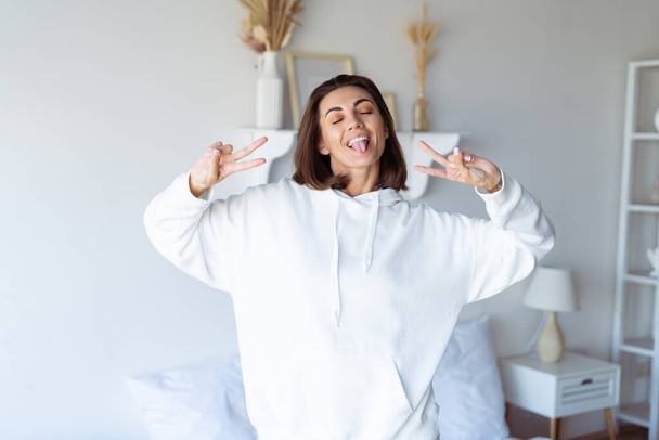 Young woman at home in the bedroom in a warm white hoodie, happy, posing, smiling, cozy winter evening - Photo, Image