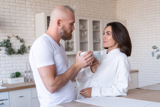 台所で妻と一緒に若い夫婦の夫、幸せな笑顔笑い、朝のコーヒーを飲む、チャット、その日の計画を議論 - 写真・画像