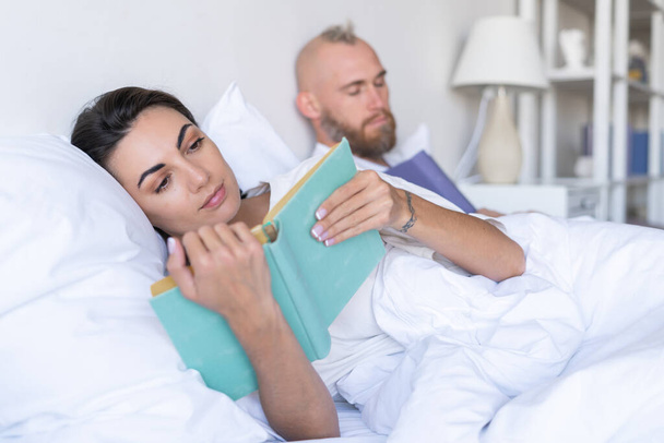 Молодая пара муж с женой дома в постели чтение книг осенью зимний вечер, мужчина заснул - Фото, изображение