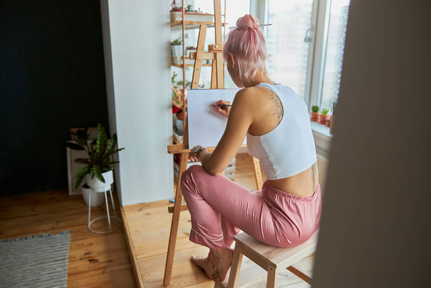 Lady artist in casual clothes at work upon picture on blank canvas at home - Photo, Image