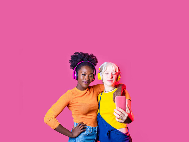 Две молодые разнообразные женщины лучшие друзья изолированы делать селфи с помощью смартфона улыбаясь счастливый и положительный изолированный рекламный фон копирайта - Фото, изображение