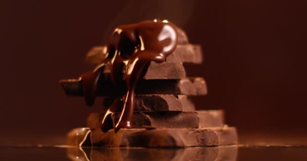 Dark melted chocolate pouring over stack of broken pieces chocolate in slow motion - Footage, Video