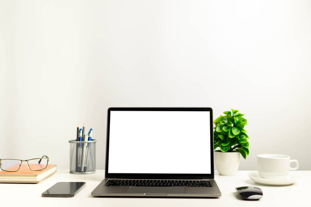 Ein funktionierendes Konzept mit Technologie, Notebook, Smartphones, Geräten. Blanker weißer Bildschirm-Laptop auf einem weißen Tisch im Büro. Kopierraum auf der Oberseite für Design oder Text, Nahaufnahme, Grau und Hintergrund verwischen - Foto, Bild