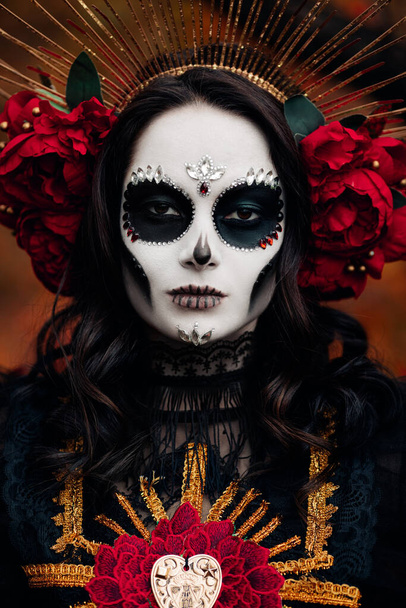Portrait of young woman with sugar skull makeup and red roses dressed in black costume of death as Santa Muerte. Day of the Dead or Halloween concept. - Foto, immagini