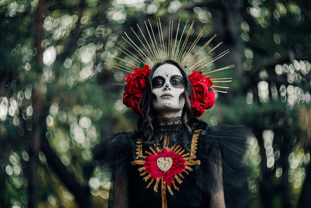Siyah ölüm kostümü giymiş, kafatası şekeri makyajlı ve kırmızı güllü genç kadın portresi Santa Muerte gibi. Ölüler Günü ya da Cadılar Bayramı konsepti. Bokeh etkisi. - Fotoğraf, Görsel