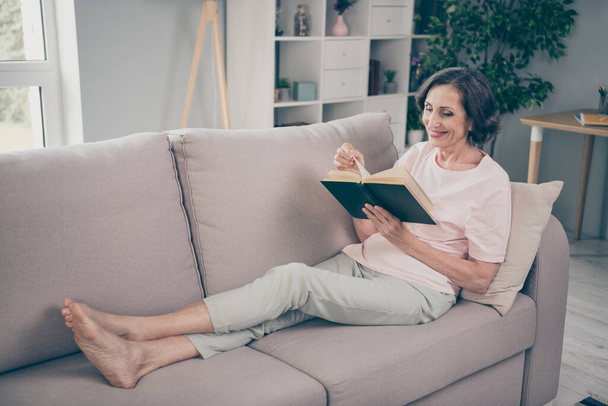 Photo of dreamy cute senior lady wear casual outfit smiling sitting couch reading book indoors house room - Foto, Imagem