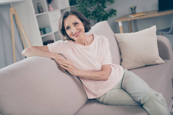 Zdjęcie dojrzałej brunetki pani siedzieć na kanapie nosić różowy t-shirt spodnie w domu sam - Zdjęcie, obraz
