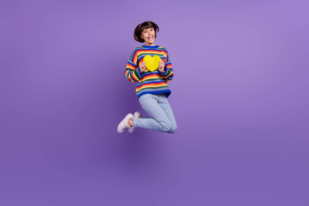 Foto inspirované flirtující dáma skok držet srdce karty nosit pruhované svetr džíny boty izolované fialové barvy pozadí - Fotografie, Obrázek