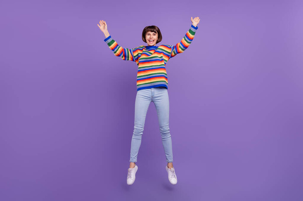 Photo of glad pretty lady jump enjoy weekend wear striped pullover jeans shoes isolated violet color background - Valokuva, kuva