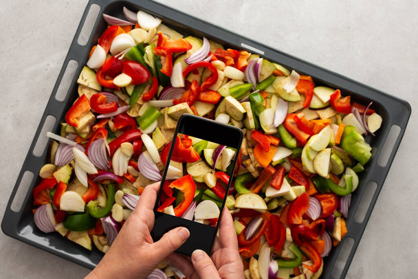 Eine erwachsene Frau macht am Telefon Fotos von Gemüsekompott für soziale Netzwerke oder einen kulinarischen Blog, von oben betrachtet, Hobby Hausmannskost, gesunder Lebensstil - Foto, Bild