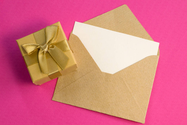 Simple small envelope with space for writing and cute small rose on wooden background with gold gift box close-up Narrow focus line, shallow depth of field high angle view - Photo, image