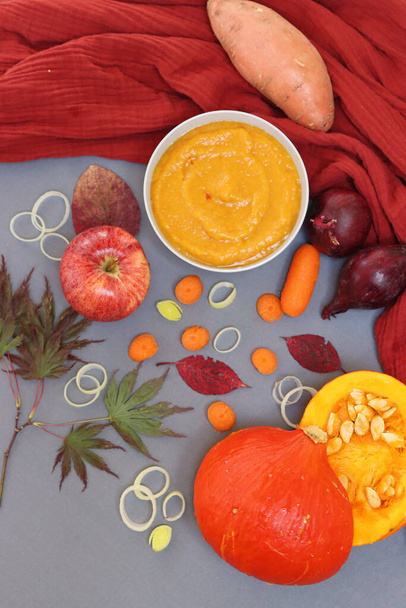 Soupe de courge crémeuse, citrouille, pomme, bébé carottes, poireau et oignon rouge sur une table. Vue de dessus de la nourriture d'automne. Concept d'alimentation équilibrée.  - Photo, image