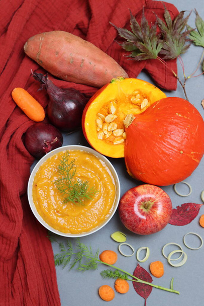 Soupe de courge au lait de coco, carotte, pomme et épices. Photo de vue du dessus de la soupe de citrouille savoureuse sur serviette de cuisine rouge. Couleurs de l'automne sur une table.  - Photo, image