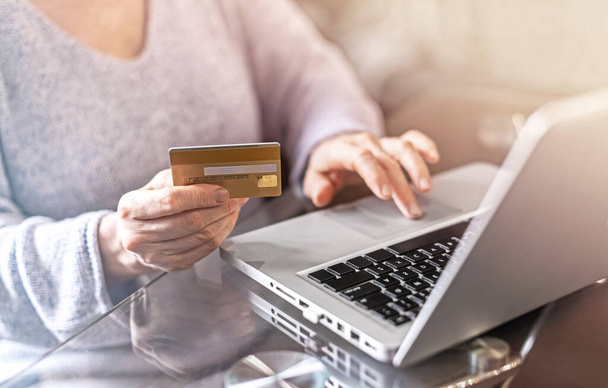 Close-up hands of an adult woman holding a credit card and using a laptop. The concept of online shopping and business online - Foto, Bild