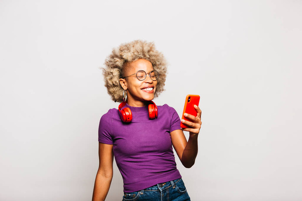 Portré mosolygó fiatal nő használ okos telefon és fejhallgató tánc ellen fehér háttér - Fotó, kép