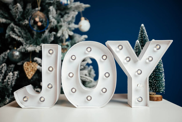 The letters JOY against blue background and Christmas tree. Holiday background.  - Фото, изображение
