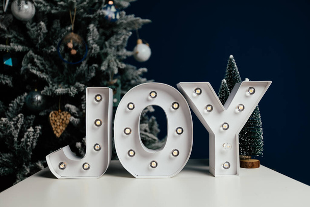 The letters JOY against blue background and Christmas tree. Holiday background.  - Foto, afbeelding