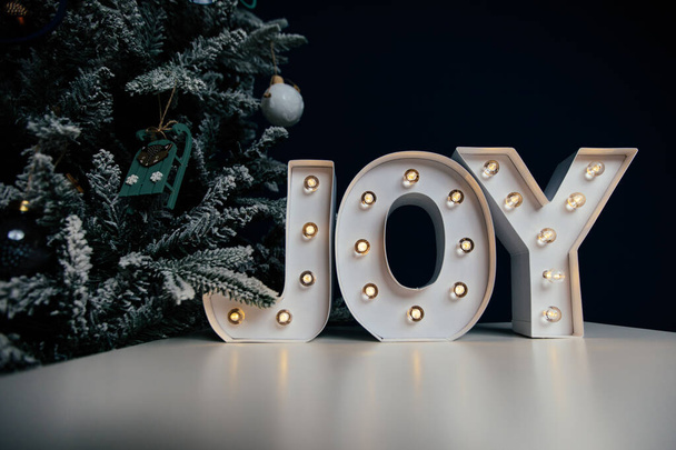 Die Buchstaben JOY vor blauem Hintergrund und Weihnachtsbaum. Hintergrund der Feiertage.  - Foto, Bild