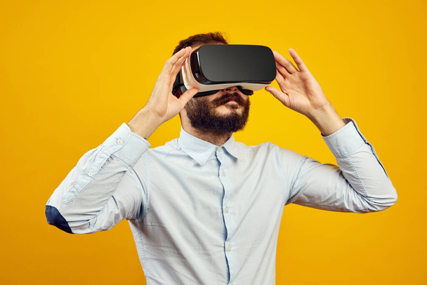 Junger Mann lächelt breit, während er ein VR-Headset auf gelbem Hintergrund trägt - Foto, Bild