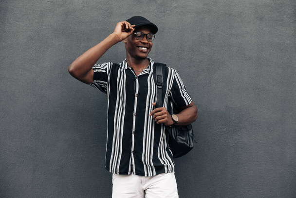 portrait of an African American man against a black wall, looking to the side, smiling broadly, wearing a shirt and shert, summer mood - Fotó, kép
