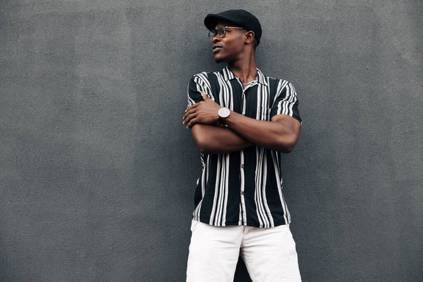 portrait of an African American man against a black wall, looking to the side, smiling broadly, wearing a shirt and shert, summer mood - Fotó, kép