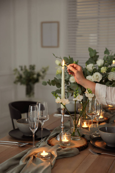 Woman lightning up candle at dining table indoors, closeup. Festive setting - Foto, Imagen