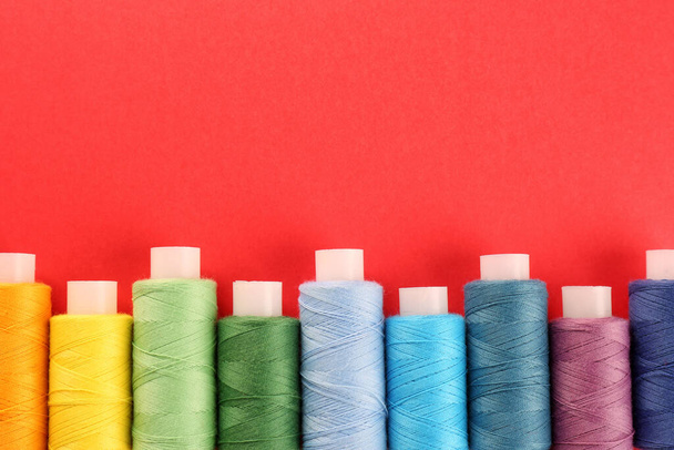 Different colorful sewing threads on red background, flat lay. Space for text - Foto, Bild