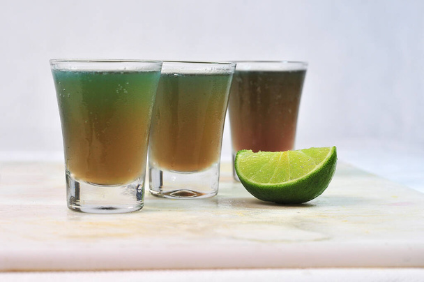 tre dosi di bevanda di assenzio, tequila e vodka con limone nella tazza di vetro sul tavolo, immagine orizzontale con sfondo sfocato - Foto, immagini