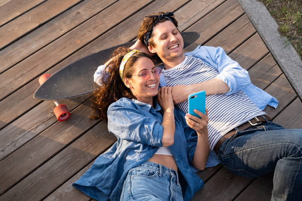 Vista superior de hombre y mujer con monopatín viendo vídeo o fotos en el teléfono inteligente - Foto, imagen