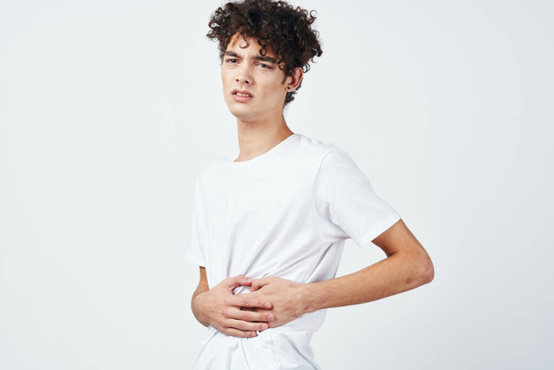 bouclé gars dans un t-shirt blanc tenant son estomac diarrhée inconfort - Photo, image