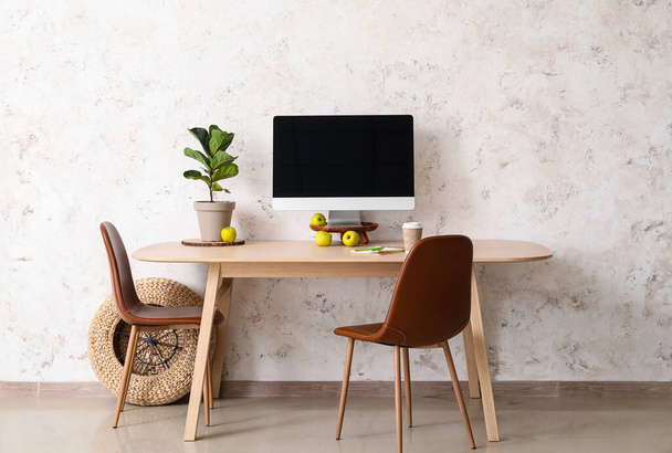 Table avec des chaises marron en cuir et ordinateur près du mur léger - Photo, image