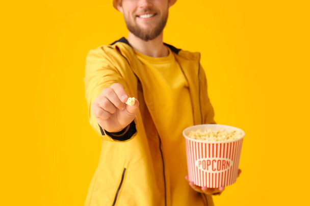 Lächelnder junger Mann zeigt Popcorn auf farbigem Hintergrund - Foto, Bild