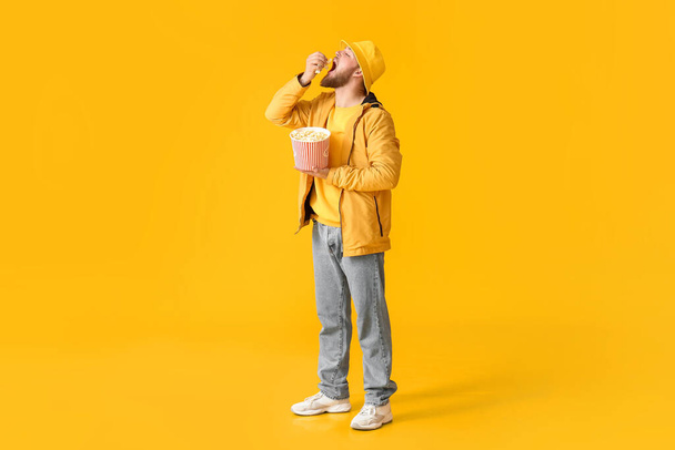 Mladý chlap jíst popcorn na barevném pozadí - Fotografie, Obrázek