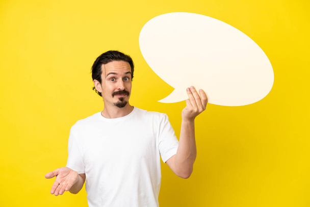 Young caucasian man isolated on yellow background holding an empty speech bubble and having doubts - Photo, Image