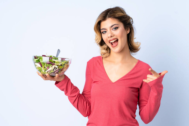 Подросток женщина с салатом изолированы на синем фоне указывая в сторону представить продукт - Фото, изображение