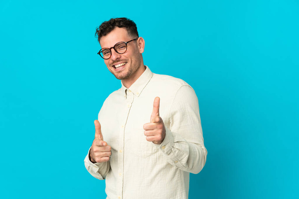 Young caucasian handsome man isolated on blue background pointing to the front and smiling - Φωτογραφία, εικόνα