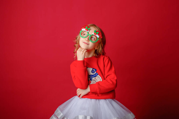 κοριτσάκι σε κόκκινο φόντο σε χριστουγεννιάτικα ποτήρια καρναβαλιού - Φωτογραφία, εικόνα