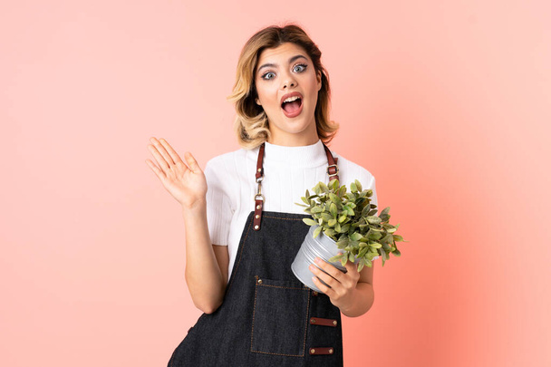 Russian gardener girl holding a plant isolated on pink background with surprise facial expression - Photo, Image