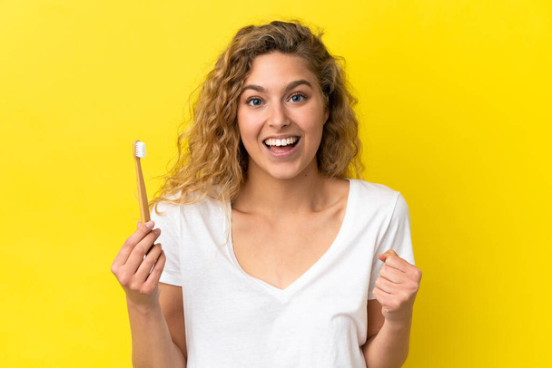 Young caucasian woman holding a brushing teeth isolated on yellow background celebrating a victory in winner position - Foto, imagen