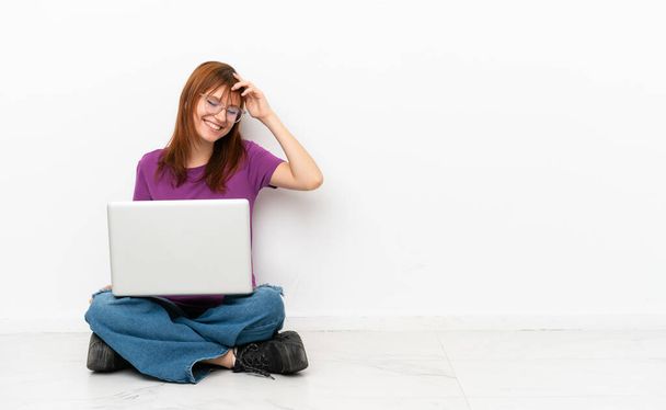Dizüstü bilgisayarı olan kızıl saçlı kız yerde oturmuş gülüyor. - Fotoğraf, Görsel