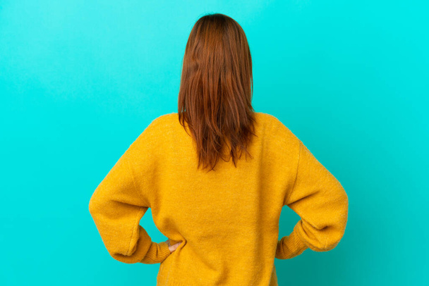 Redhead girl isolated on blue background in back position - Фото, зображення