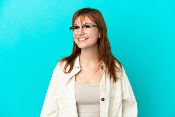 Piros lány elszigetelt kék háttér szemüveggel boldog arckifejezéssel - Fotó, kép