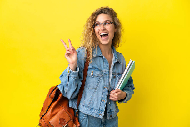 Young student caucasian woman isolated on yellow background smiling and showing victory sign - Photo, Image