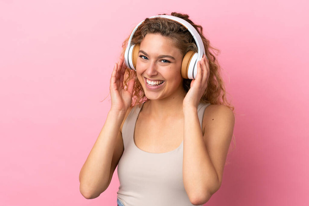 Young blonde woman isolated on pink background listening music - Fotó, kép