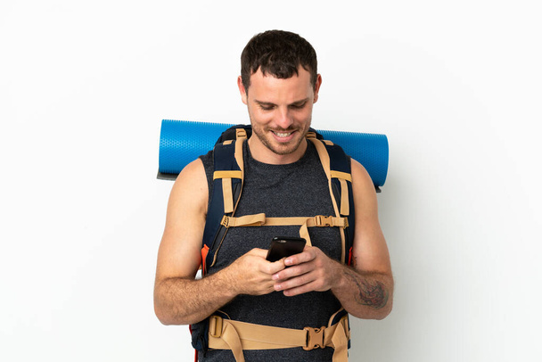 Бразильський альпініст з великим рюкзаком через ізольований білий фон надсилає повідомлення мобільним телефоном - Фото, зображення