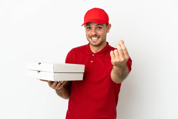 Доставщик пиццы в рабочей форме подбирает коробки пиццы над изолированной белой стеной, зарабатывая деньги. - Фото, изображение