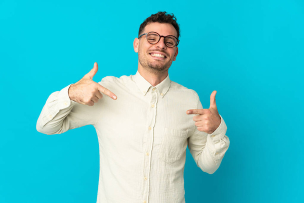 Young caucasian handsome man isolated on blue background proud and self-satisfied - Photo, Image
