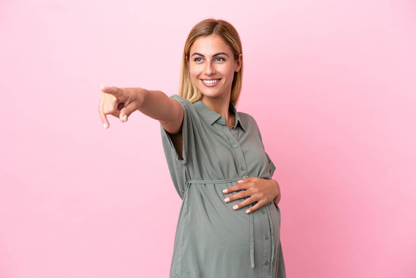 Jonge Uruguayaanse vrouw geïsoleerd op blauwe achtergrond zwanger en wijzend naar het front - Foto, afbeelding